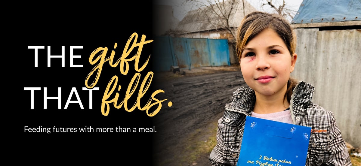 Email header image with "The Gift That Fills" wordmark and the tagline "Feeding futures with more than a meal." The photo is of one of the Ivanenko children holding a Christmas book.