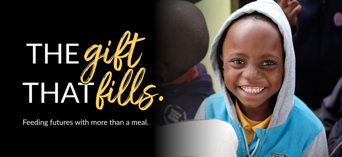 A little boy smiling at a Rise Against Hunger meal distribution site. The Gift That Fills wordmark with the tagline: "Feeding futures with more than a meal." 