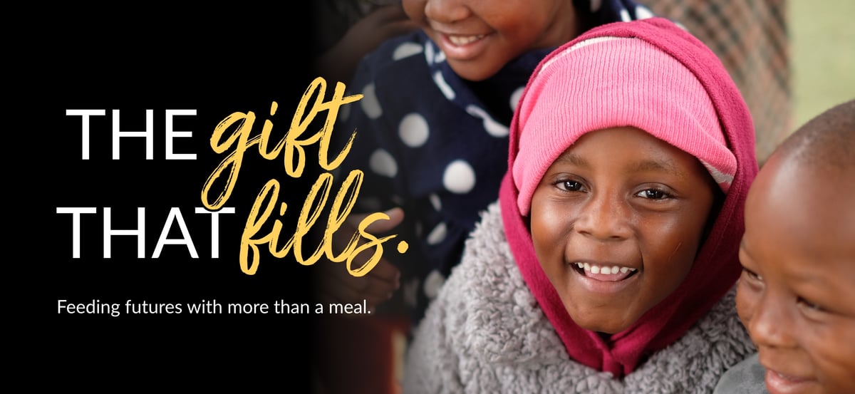 The wordmark "The Gift That Fills" with tagline "Feeding futures with more than a meal." A photo of a young girl surrounded by her peers.