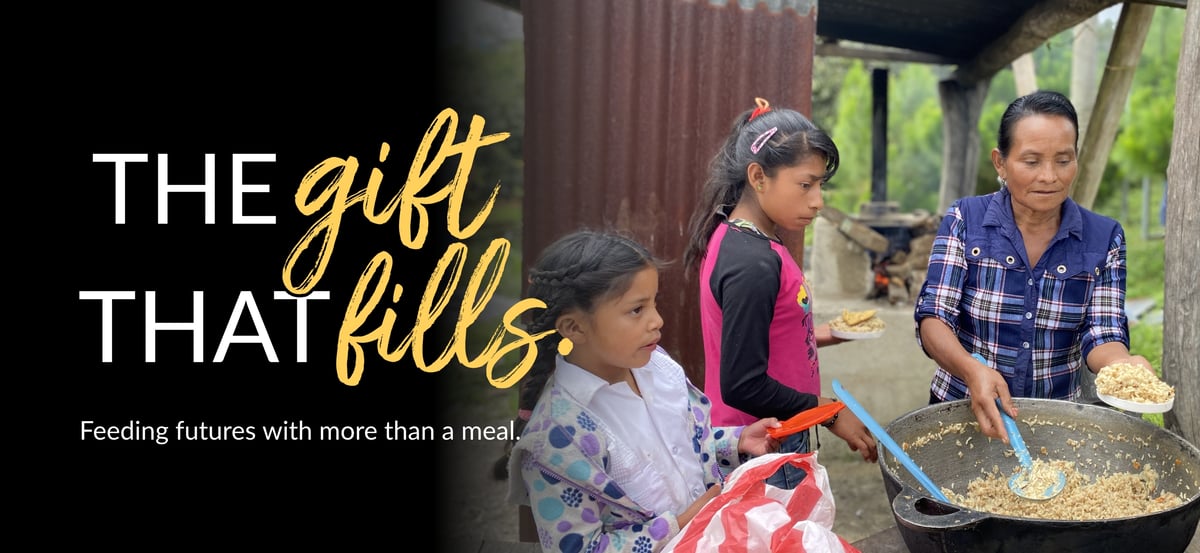 Email header image with "The Gift That Fills" wordmark and the tagline "Feeding futures with more than a meal." The photo is of children receiving Rise Against Hunger meals prepared by a woman in their community.